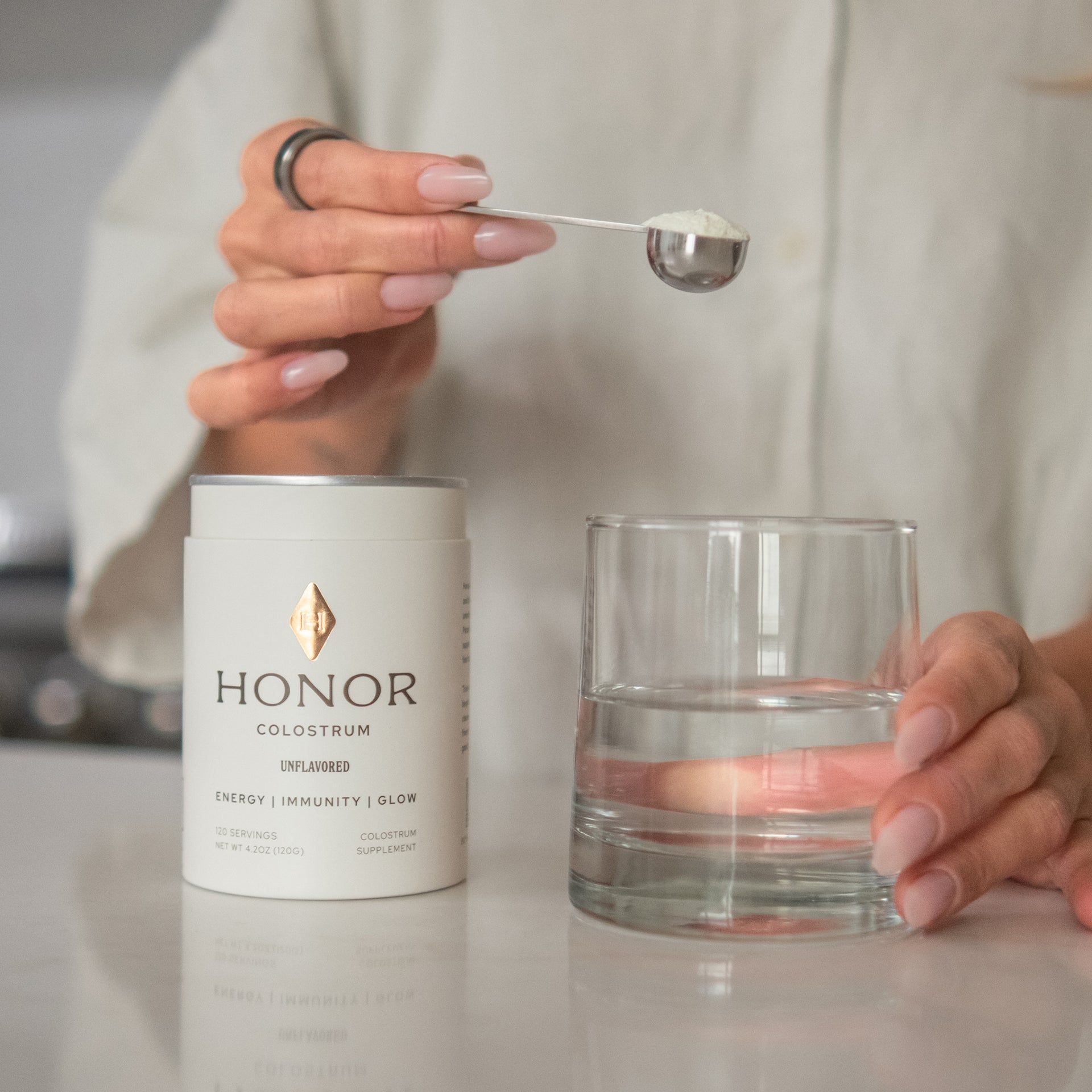 Scooping Honor Colostrum powder into a glass of water